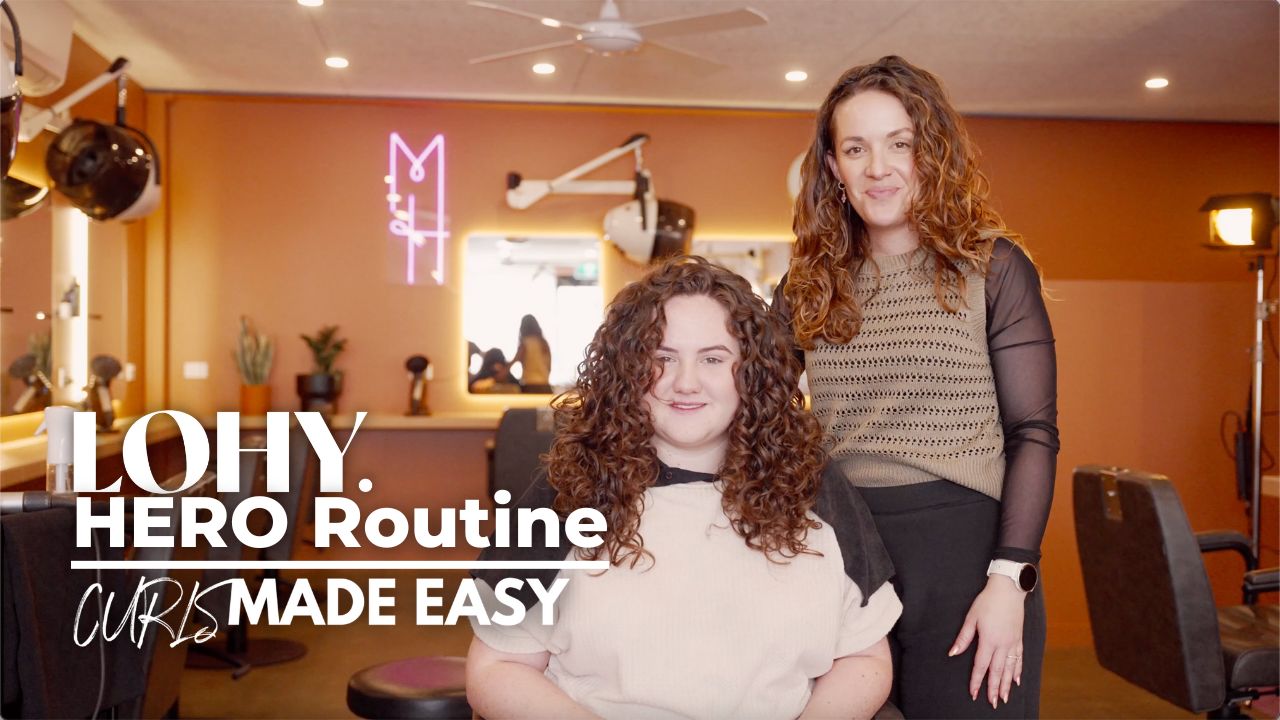 text saying "LOHY. HERO Routine Curls Made Easy", woman with wavy brunette hair, sitting in salon chair looking towards camera, and Jonina from LOHY. standing behind chair with wavy brunette hair