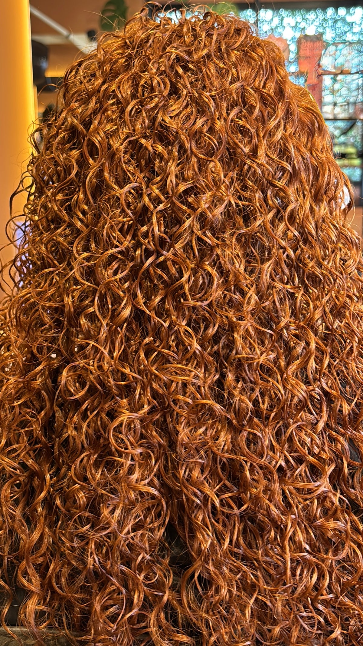 A close-up view of a voluminous, tightly curl pattern with a warm coppery auburn color, filling the frame.