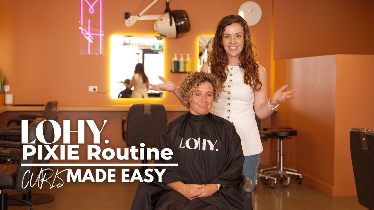 text saying "LOHY. PIXIE Routine Curls Made Easy", woman with short curly blonde hair, sitting in salon chair looking towards camera, and Jonina from LOHY. standing behind chair with wavy brunette hair smiling.