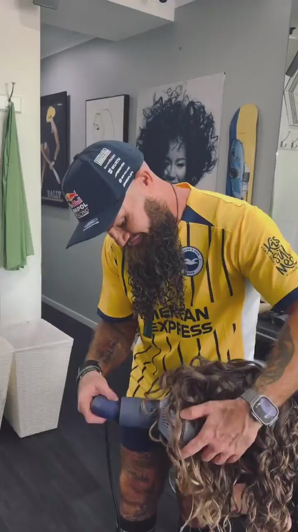 Load video: Male hairdresser in a yellow shirt drying hair with the diffuser