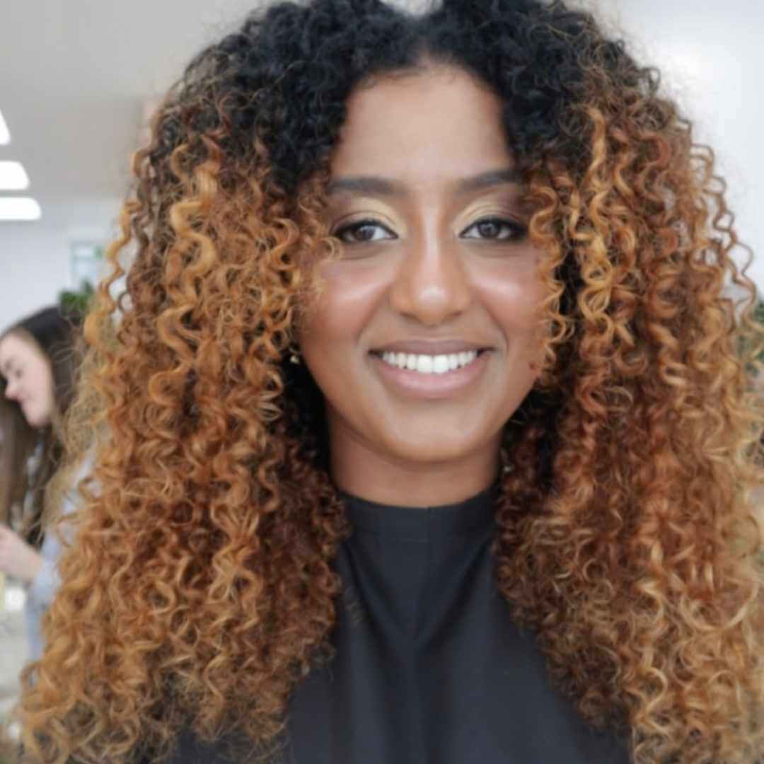 woman with voluminous black and blonde 3c curly hair smiling